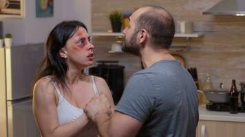 Furious couple hitting each other in the kitchen. Abused terrified beaten wife covered in bruises suffering injury from alcoholic violent brutal aggressive husband screeming, fighting. photo