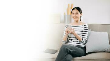 Young asian woman using smartphone and tablet while seated on couch at home photo