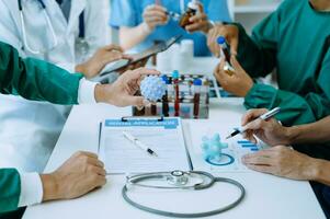 Medical team having a meeting with doctors in white lab coats and surgical scrubs seated at a table discussing a patients working online using computers in the medical industry photo