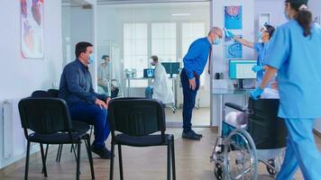 Nurse with face mask for covid19 in hospital waiting area checking senior man temperature with temperature scanner. Assistant helping invalid senior woman in wheelchair. photo