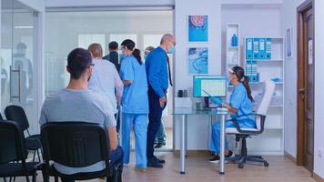 Medic with visor against covid 19 calling patient in consultation room. Senior man with face mask in hospital waiting room talking with nurse. Disabled woman with zimmer frame. photo