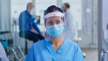 Medical assistant with visor and face mask against coronavirus looking at camera in hospital waiting area. Doctor consulting senior man in examination room. photo