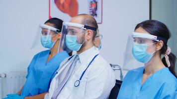 Medical personnel with face mask and visor against coronavirus sitting on chairs in hospital waiting area. Medic wearing stethoscope. photo