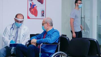 Doctor with face mask and stethoscope consulting disabled senior man in hospital waiting area. Medical staff wearing protection against infection with coronavirus. Old woman entering in clinic. photo