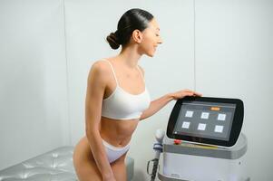 Young beautiful woman with laser hair removal machine in cosmetology cabinet photo