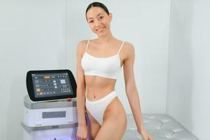 Young beautiful woman with laser hair removal machine in cosmetology cabinet photo