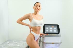 Happy woman near the laser hair removal machine. Beauty studio photo