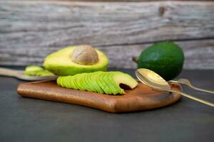 halved and finely sliced avocado on wooden plate on black background. photo