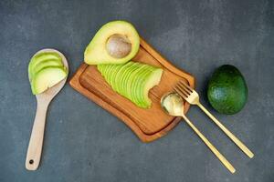 Top view of halved and finely sliced avocado on wooden plate on black background. photo