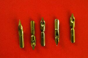 five gold pen nibs on a red surface photo