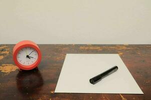 a red alarm clock and a white sheet of paper on a table photo