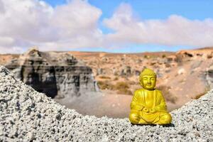golden buddha statue on a gravel cliff in the desert photo