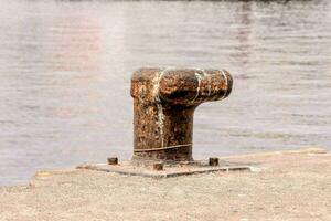 a rusty metal post on the edge of the water photo