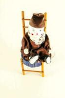 a small doll sitting on a wooden chair photo