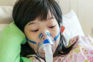 Sick little asian girl inhalation with nebulizer for respiratory treatment photo