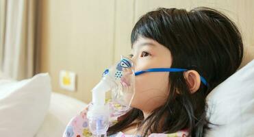 Sick little asian girl inhalation with nebulizer for respiratory treatment photo