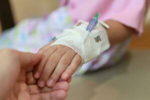 Mother holding child hand with saline IV solution in hospital photo