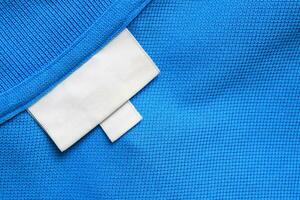 Blank white laundry care clothes label on blue shirt fabric texture background photo