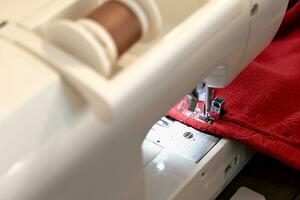 Man using a sewing machine with a red garment, for repair work, customization, creation, upcycling photo