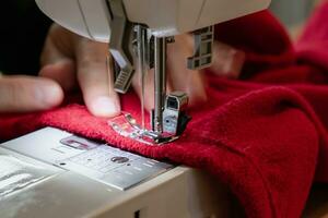 hombre utilizando un de coser máquina con un rojo prenda, para reparar trabajar, personalización, creación, reciclado foto
