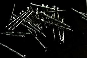 The screws are placed on a black wooden table with lighting from the side. photo