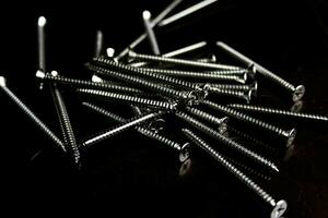 The screws are placed on a black wooden table with lighting from the side. photo