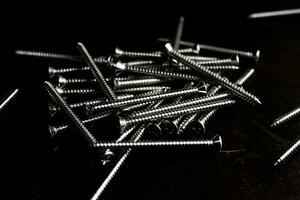 The screws are placed on a black wooden table with lighting from the side. photo