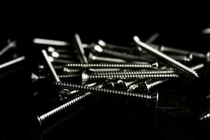 The screws are placed on a black wooden table with lighting from the side. photo