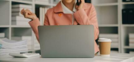 Attractive smiling young asian business woman work at home office, Asian woman working on laptop computer holding tablet. photo