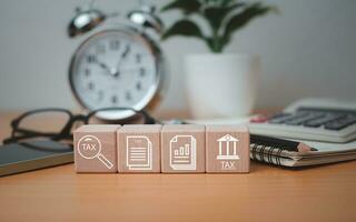 Wooden block printed tax symbols icons placed on a wooden tabletop with office supplies, financial research, reports, tax return calculations. photo