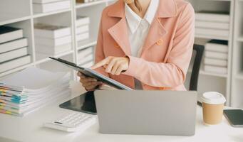 Attractive smiling young asian business woman work at home office, Asian woman working on laptop computer holding tablet. photo