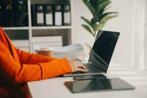 Attractive smiling young asian business woman work at home office, Asian woman working on laptop computer holding tablet. photo