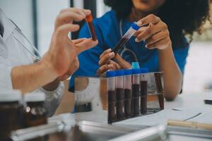 Medical worker in lab coat and sterile mask, doing a microscope analysis while her colleague are working behind photo