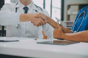 Doctor and patient shaking hands in the office, they are sitting at desk, hands close up photo