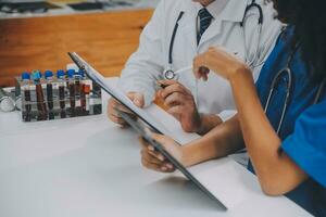 Medical worker in lab coat and sterile mask, doing a microscope analysis while her colleague are working behind photo