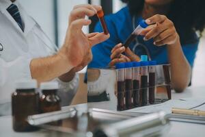 Medical worker in lab coat and sterile mask, doing a microscope analysis while her colleague are working behind photo