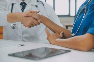 Doctor and patient shaking hands in the office, they are sitting at desk, hands close up photo