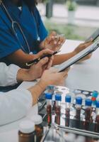 Medical worker in lab coat and sterile mask, doing a microscope analysis while her colleague are working behind photo