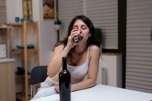 Unhappy woman with alcohol addiction drinking wine alone feeling depressed and intoxicated. Young adult with bottle of wine and glass using liquor for sadness, loneliness and desperation photo