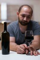 Close up of bottle and glass of wine prepared for man feeling unhappy and lonely. Person drinking alcoholic beverage, booze, liquor while being alone in kitchen. Intoxicated adult photo