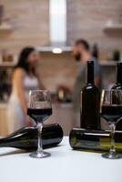 Close up of empty bottles of alcoholic beverage and glasses with wine on kitchen counter. Liquor and booze prepared for intoxicated couple with alcohol addiction sitting in background photo