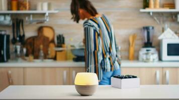 Essential oils diffuser distributing aromatherapy while woman walks in the kitchen. Aroma health essence, welness aromatherapy home spa fragrance tranquil theraphy, therapeutic steam, mental health treatment photo
