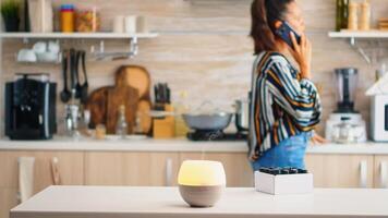 Woman talking on the phone with essential oils aromatherapy next to her in the kitchen. Aroma health essence, welness aromatherapy home spa fragrance tranquil theraphy, therapeutic steam, mental health treatment photo