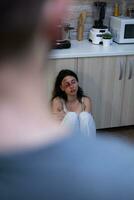 Domestic violence victim sitting on floor because of social problems. Abusive husband beating terrified helpless wife with bruises on face. Woman with physical trauma, aggression photo