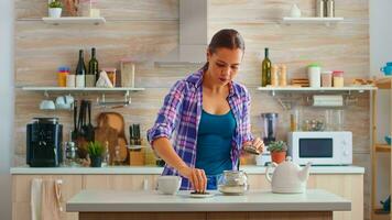 Young woman preparing green tea for breakfast in a modern kitchen using teapot sitting near the table. Putting with hands, pressing herbal, healthy, tea leaves, in pot, in the morning. photo