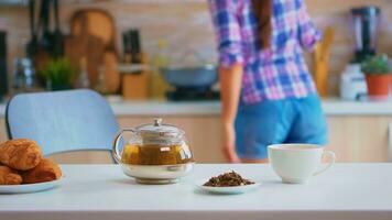 joven mujer preparando el desayuno con cuerno y verde té. Disparo con antecedentes difuminar de dama teniendo genial Mañana con sabroso natural sano herbario té sentado en el cocina. foto