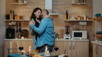 Cheerful young couple dancing and kissing during romantic dinner. Happy in love couple dining together at home, enjoying the meal, celebrating their anniversary. photo