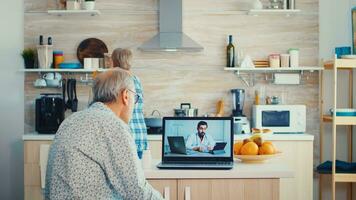 Senior couple during video conference with doctor using laptop in kitchen discussing about health problems. Online health consultation for elderly people drugs ilness advice on symptoms, physician telemedicine webcam. Medical care internet chat photo