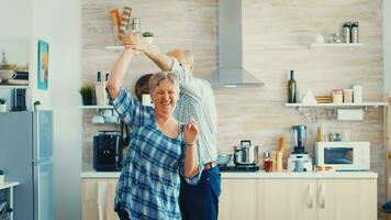 Joyful old old man and woman dancing in kitchen. Happy senior couple having fun, retired persons in cozy home enjoying life photo