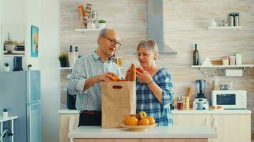 Senior couple arriving from supermarket with grocery bag and unpacking in kitchen. Elderly retired persons enjoying life, spending time helping each other photo